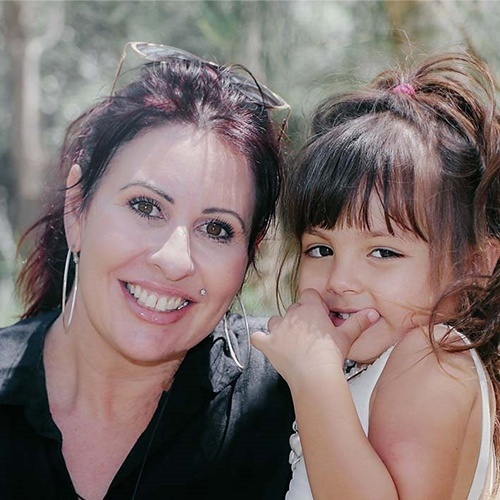 A photo of our First Nation Photographer Nonnie with her daughter. Nonnie has round earrings and is wearing a black tshirt. Her daughter is smiling and has a white dress.