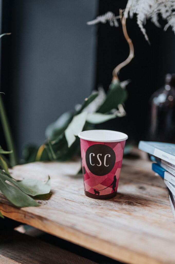 A coffee cup sitting on a desk with an Aboriginal artwork on it and 'CSC' written in the middle.