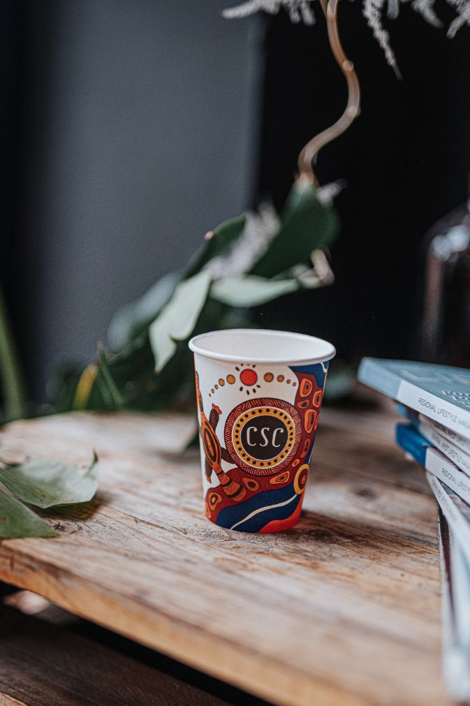 A coffee cup sitting on a desk with an Aboriginal artwork on it and 'CSC' written in the middle.