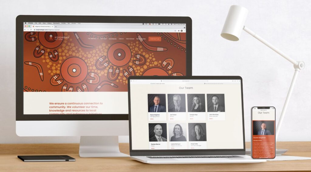 A desktop computer and laptop sitting on a desk displaying a website with an orange Aboriginal artwork and a team of people.