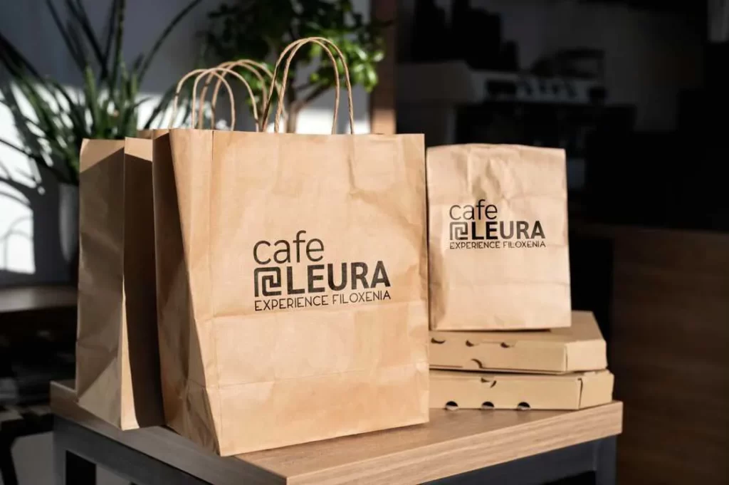 Two brown paper bags with the Cafe Leura Experience Filoxenia logo on it.
