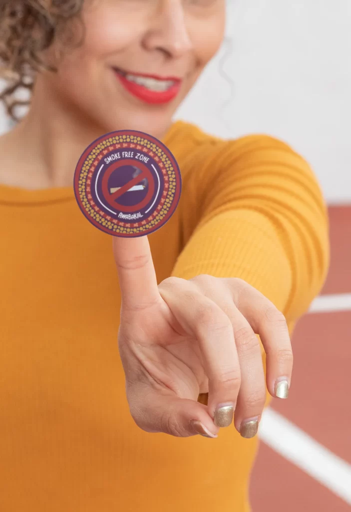 A woman holding a Smoke Free Zone Awabakal sticker with an Aboriginal design