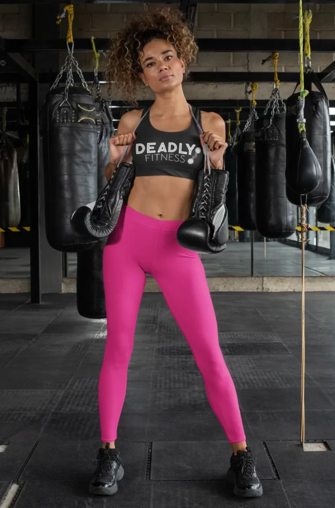 A woman in a gym holding boxing gloves. Her sports bra has the Deadly Fitness logo on it.