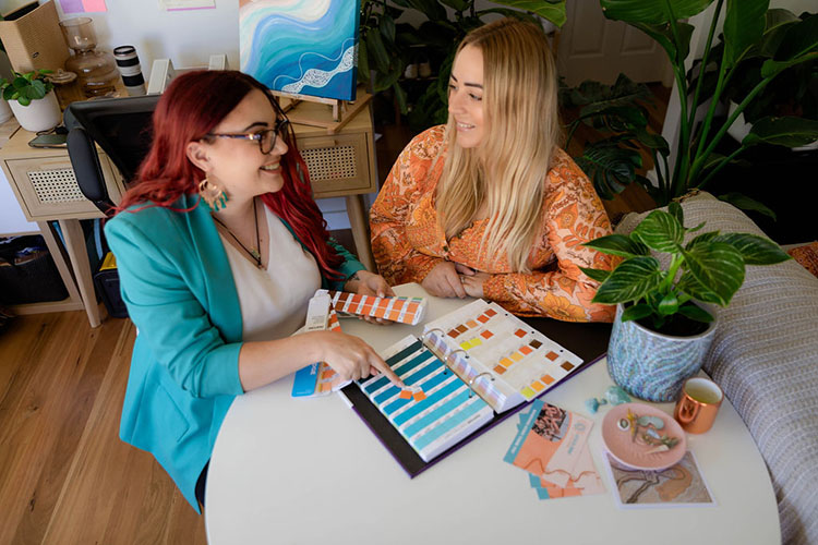 A photo of two girls sitting around a desk looking at colours